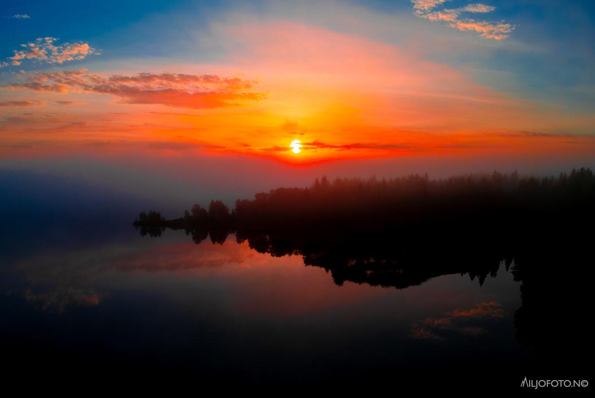 Solnedgang over sjø og skog